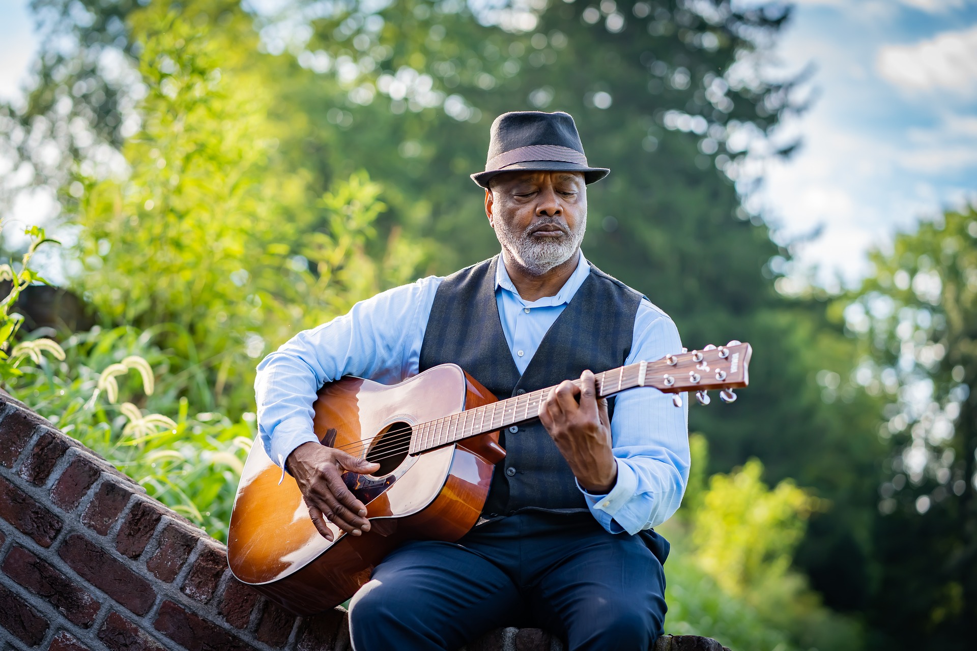 Man playing guitar outdoors in a hat and vest
